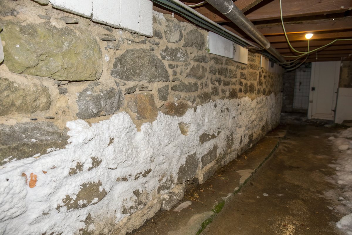 White crusty efflorescence and a damp band across an old fieldstone basement wall
